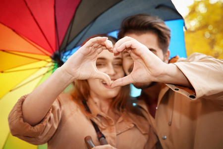一对幸福的夫妇，带着五颜六色的雨伞，用手在公园里做心