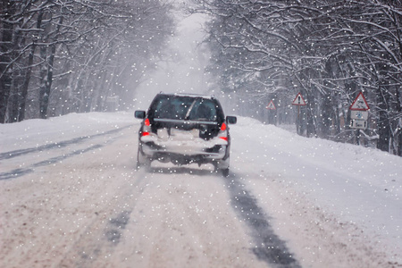 在大雪纷飞的冬季道路上，在冰天雪地的森林中移动汽车。 天气寒冷，暴风雪，能见度差，道路滑。 莫斯科地区。