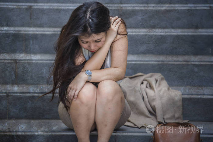 年轻的沮丧和绝望的亚裔美国女商人独自哭泣,坐在街道楼梯上,承受着