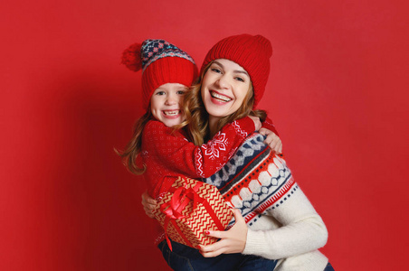 幸福的家庭母亲和孩子女儿带着红色背景的圣诞礼物和帽子