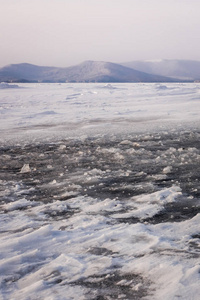天然冬湖破冰，晴空背景选择性聚焦。 冰冻的山湖，表面有蓝色的冰和裂缝。 蓝天下雪山的冬季景观。