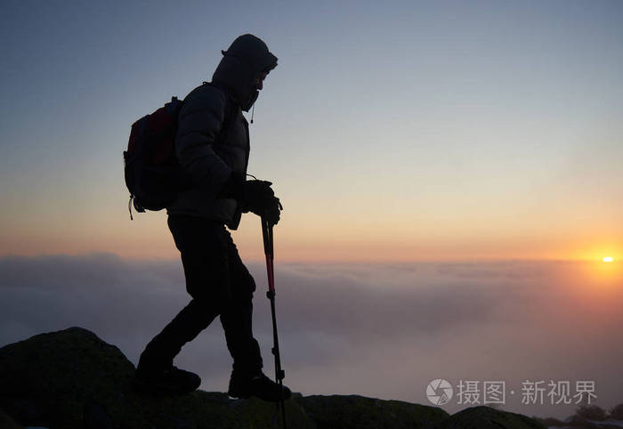 旅行者徒步旅行者的剪影背包和徒步旅行棒在岩石山峰上背面有雾云