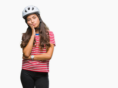 年轻的阿拉伯骑自行车的女人戴着安全帽，在孤立的背景下思考，看起来疲惫，厌倦了交叉双臂的抑郁问题。
