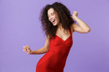 20岁的快乐女人穿着红色连衣裙，微笑着，在紫罗兰的背景下跳舞