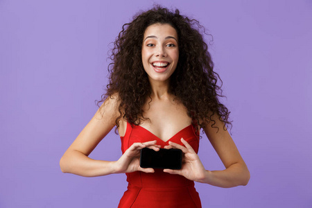 微笑的女人20多岁，穿着红色连衣裙，手里拿着黑色智能手机，站在紫罗兰的背景上