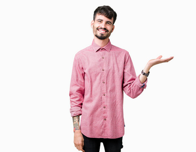 年轻的帅哥穿着粉红色的衬衫，在孤立的背景上微笑，欢快的呈现，用手掌指着相机。