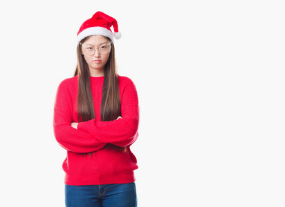 年轻的中国女人在孤立的背景下戴着圣诞帽，怀疑和紧张的表情，脸上交叉的手臂。 消极的人。