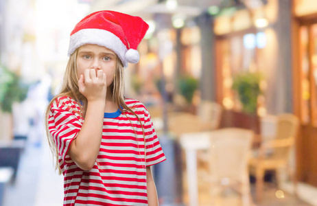 年轻漂亮的女孩戴着圣诞帽，戴着孤立的背景，看上去压力很大，紧张，双手咬着嘴的指甲。 焦虑问题。