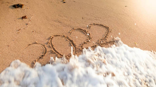 在岛屿海滩上的湿沙上写着的海浪滚动超过2022年新年数字的特写镜头照片。新年圣诞节和寒假旅行的概念