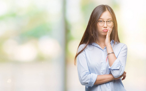 年轻的亚洲商界女性戴着眼镜，在孤立的背景下思考，看起来疲惫，厌倦了交叉双臂的抑郁问题。