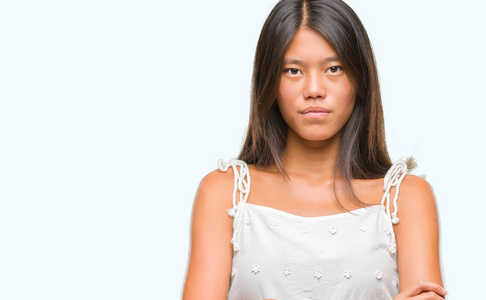 年轻的亚洲女人超过孤立的背景怀疑和紧张的不赞成的表情在脸上交叉的手臂。 消极的人。