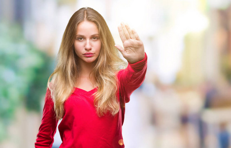年轻漂亮的金发女人穿着红色毛衣，在孤立的背景上做停止用手掌唱歌。 警告表情，脸上有负面和严肃的手势。