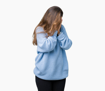 年轻美丽的黑发女人穿着蓝色的冬季毛衣，在孤立的背景上，悲伤的表情覆盖着脸，双手哭泣。 抑郁的概念。