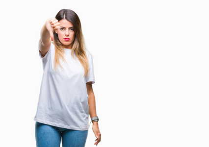 年轻漂亮的女人随意的白色T恤在孤立的背景上看起来不高兴和愤怒，表现出拒绝和消极的拇指向下的手势。 不好的表情。