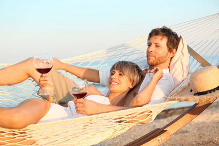 年轻夫妇在海滩上的吊床上端着酒杯休息
