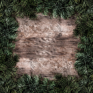创意布局框架由圣诞杉木树枝在木制背景。 圣诞节和新年主题。 平躺式顶部视图