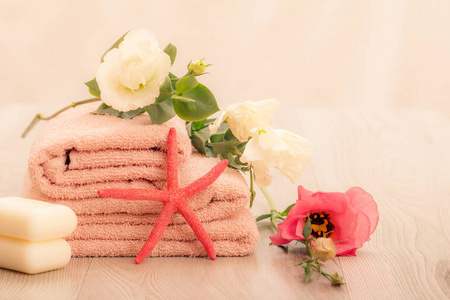 一叠柔软的特里毛巾与白色和红色的花皂和海星在粉红色的背景。 水疗产品。
