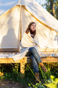 年轻女子坐在帆布帐篷附近, 把毯子盖在自己身上