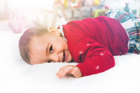 圣诞快乐。 快乐的小孩穿着一件有趣的圣诞毛衣，躺在甜蜜的家里的白色毯子上。