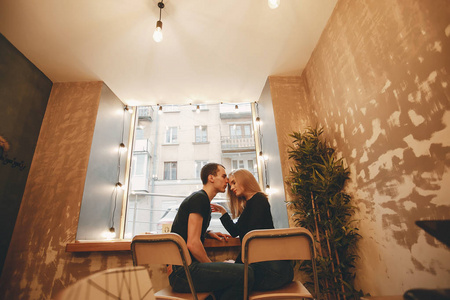一个身穿黑色T恤的金发美女和她的男朋友坐在桌旁的咖啡馆里