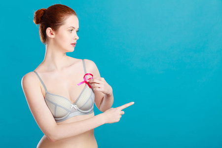 保健，医学和乳腺癌的认识理念..戴着粉色丝带的女人用手指指着胸前的蓝色