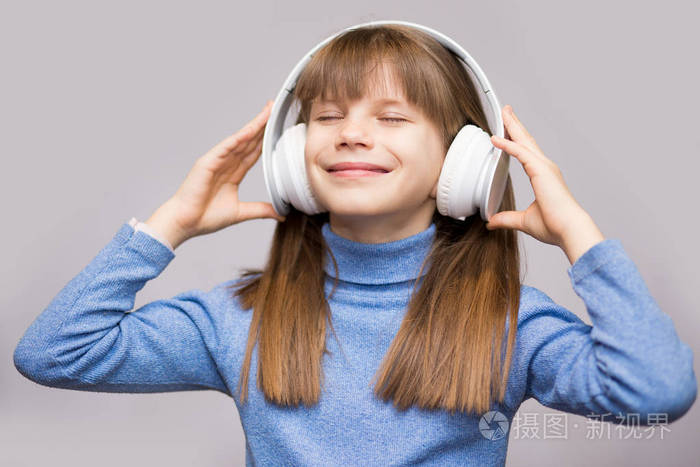 精力充沛的女孩带着耳机听音乐,闭着眼睛在白色背景上在工作室.