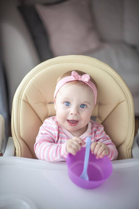 s chair and holds a spoon. Portrait of a baby with blue eyes in 