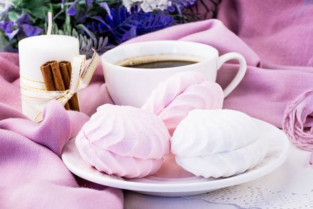 轻轻的粉红色和白色棉花糖关闭在背景，蜡烛和肉桂咖啡在一个白色的杯子。 背景中有模糊颜色的粉红色背景