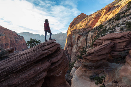 在一个充满活力的日落中，悬崖边的冒险女孩正在峡谷中美丽的风景。 摄于美国犹他州锡安国家公园。