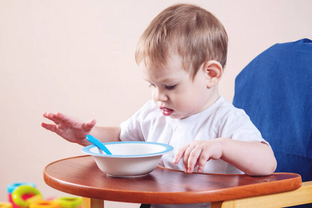 小可爱的小男孩学着在孩子桌上吃饭，在厨房里学着盘子和勺子