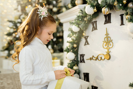 穿着白色毛衣的漂亮小女孩手里拿着礼物坐在圣诞树附近