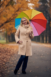 迷人的高级女人在秋天带着五颜六色的雨伞在公园里散步。