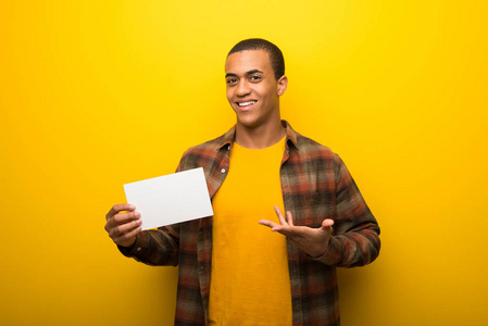 年轻的非裔美国男人，在充满活力的黄色背景上，拿着一张空的白色标语牌，插入一个概念