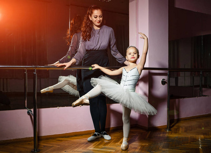 漂亮的芭蕾舞老师在舞蹈课上看芭蕾舞演员站在漂亮的姿势上。 一个小女孩和她的教练在芭蕾舞学校从事舞蹈。