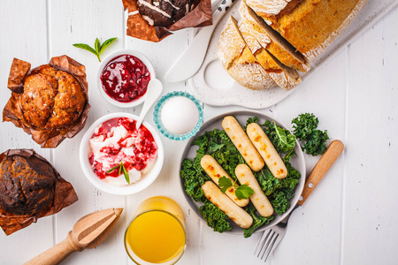 早餐提供松饼，烤香肠，果汁，新鲜面包和馅饼，在白色的木制桌子顶部观看。