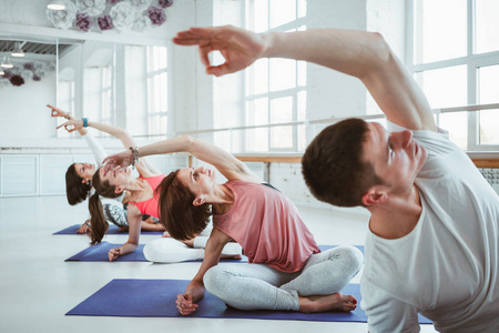 适合成年女性和男性在健身课上练习瑜伽姿势。 一群健康强壮的人在白色健身房做健身运动。 保健和生活方式