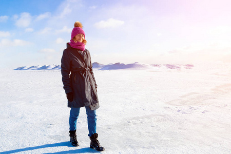 一位穿着温暖外套和帽子的年轻女子喜欢冬天的大自然，在寒冷的晴天在雪山蓝天和阳光的背景下在雪地上散步和聊天