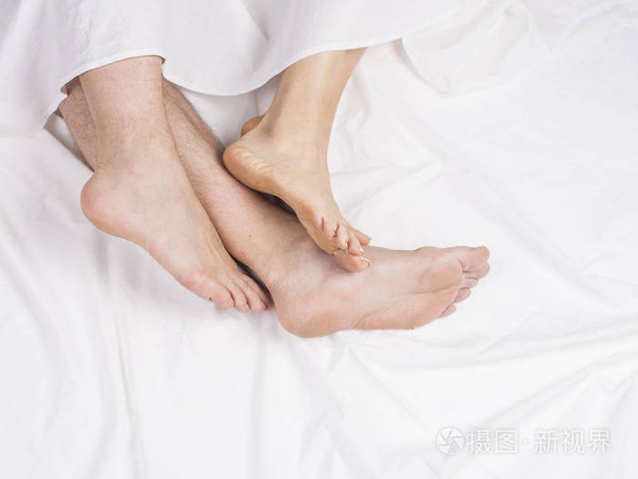 双脚并排睡在舒适的床上在白色毯子下的床上闭上脚一个男人和一个女人