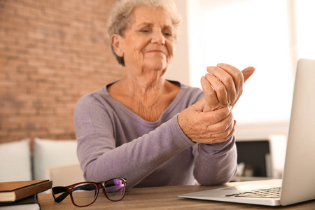戴手提电脑坐在桌旁时手腕疼痛的老年妇女