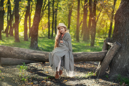 日落时留着长发的漂亮女孩在森林里。 一个女孩的肖像。 裹在毯子里的孩子