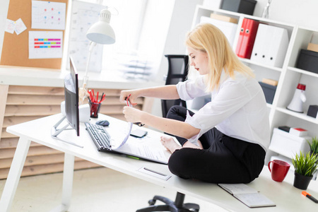 一个年轻女孩坐在办公室的桌子上, 拿着文件和电脑工作