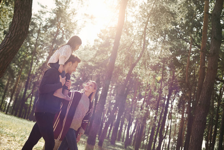 年轻的父母带着小女儿在秋林里。侧视图
