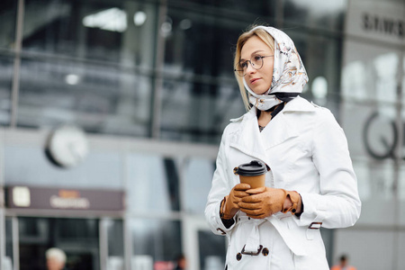 成功的商业女性的肖像，手里拿着一杯热饮料，在去城市街道工作的路上。 办公楼附近有咖啡杯的漂亮女人。