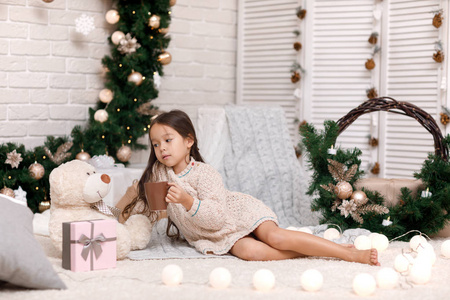 可爱的女孩喝热可可, 并发挥与泰迪熊在家里。圣诞节
