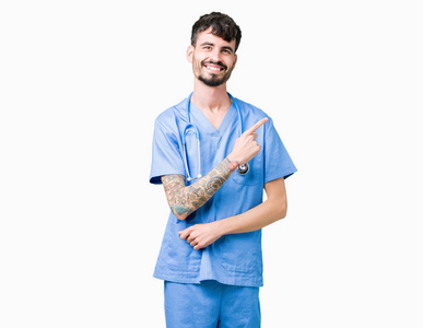 年轻英俊的护士穿着外科医生制服，背景开朗，微笑着用手和手指指向一边，脸上有快乐和自然的表情