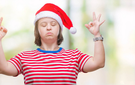 患有唐氏综合症的年轻成年妇女戴着圣诞帽，在孤立的背景上放松，闭着眼睛微笑，用手指做冥想手势。 瑜伽概念。