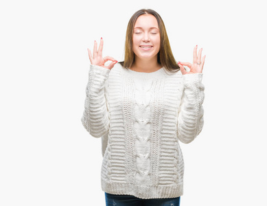 年轻美丽的白种人女人穿着冬天的毛衣，在孤立的背景下放松，微笑着闭着眼睛，用手指做冥想的手势。瑜伽概念。