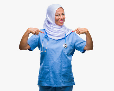中年高级阿拉伯护士妇女戴着头巾，在孤立的背景上看着自信，脸上带着微笑，手指着自己，骄傲和快乐。