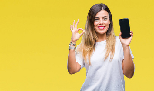 年轻漂亮的女人在孤立的背景上显示智能手机的空白屏幕，用手指做OK标志，极好的符号