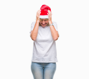 中年金发女人戴着圣诞帽，在孤立的背景下，因为疼痛和偏头痛而感到头痛绝望和压力。 手放在头上。